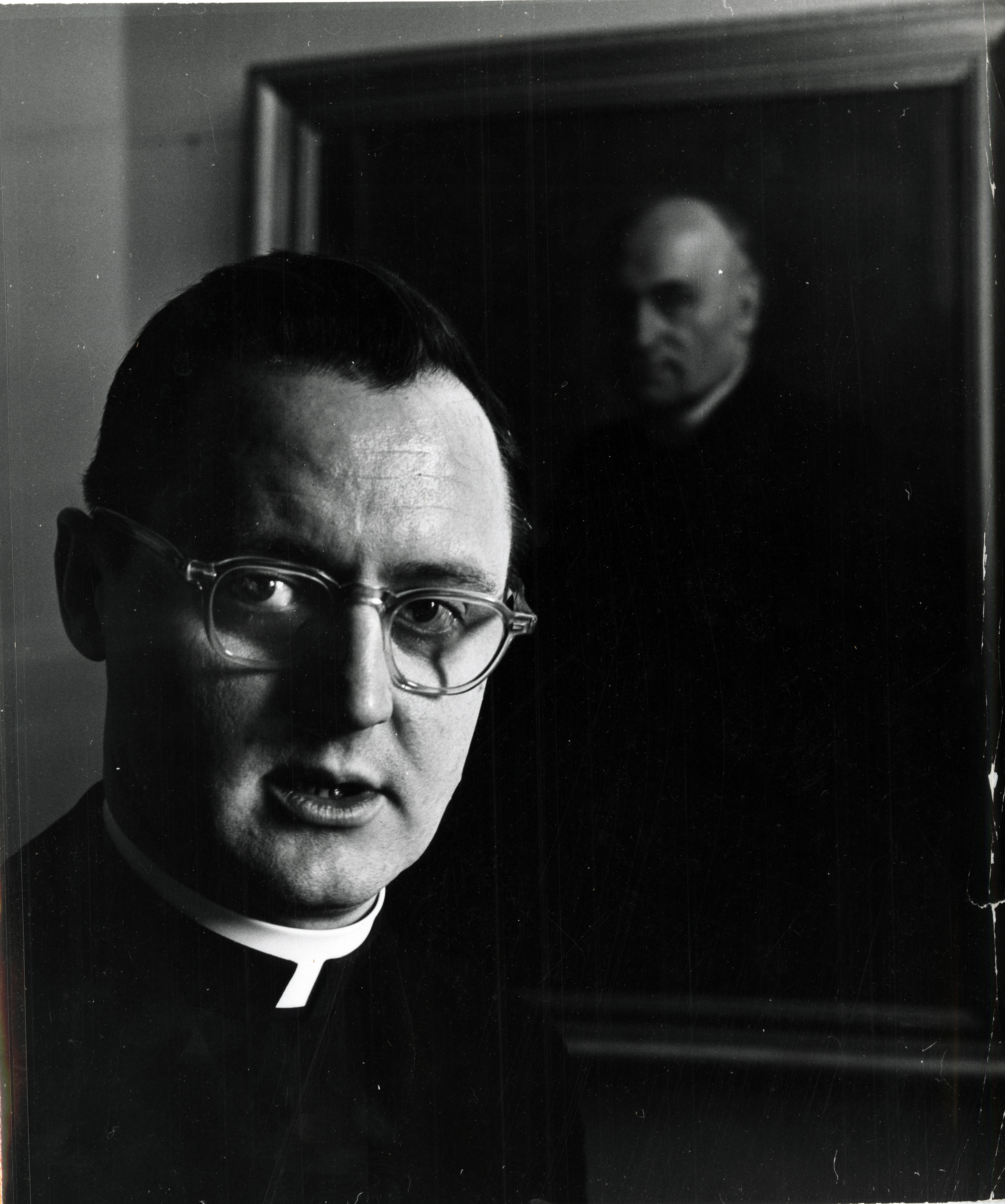 Image of Father George Higgins, with portrait of Father John A. Ryan in the background. Both ran the Social Action Department of the Bishops' Conference, a locus of Pluralist Catholic Americanism.